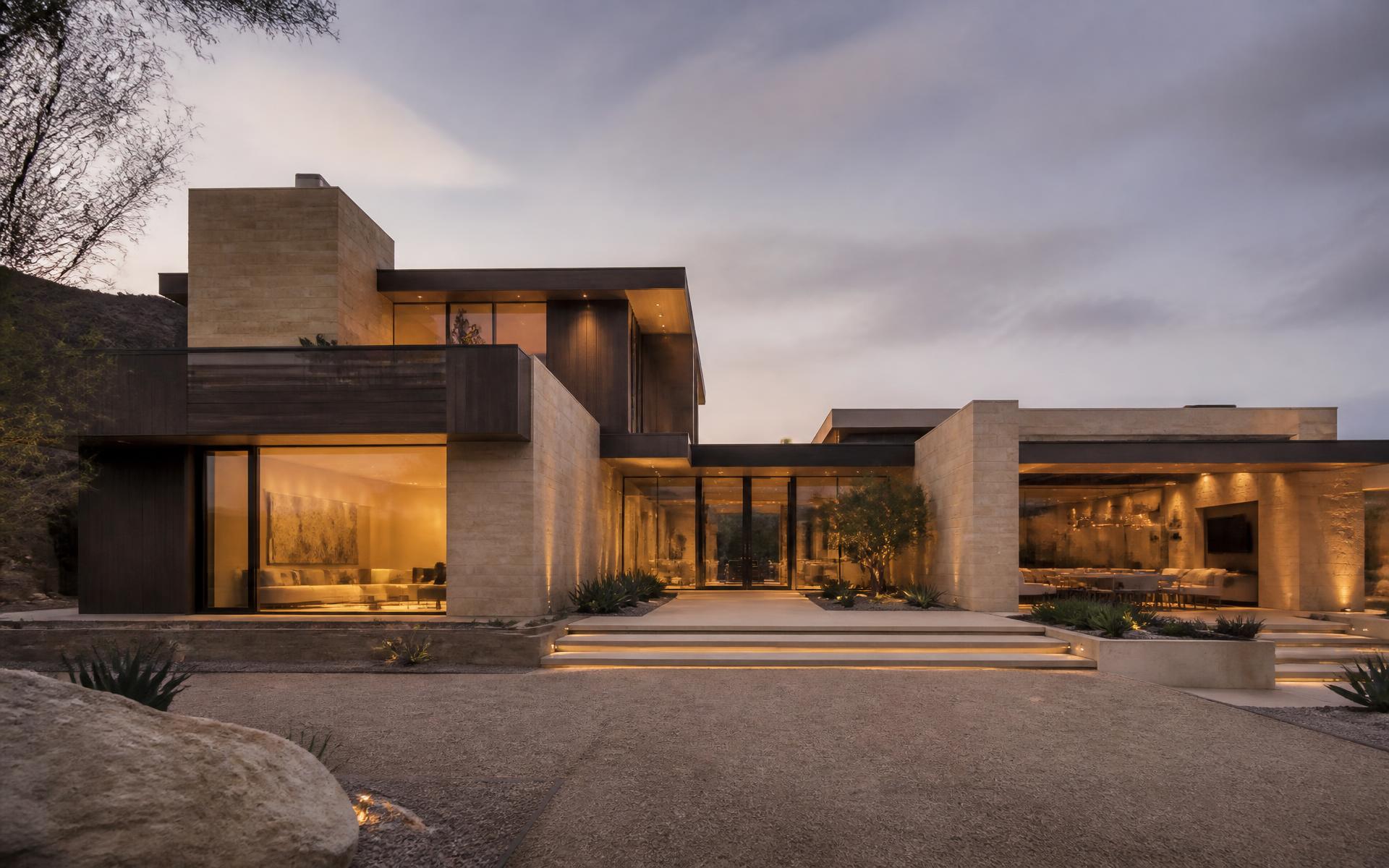 Residência contemporânea em travertino e madeira escura ao entardecer